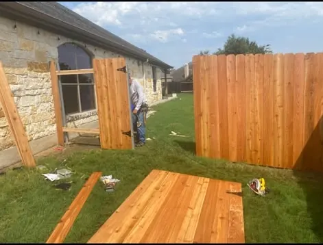 Cedar fence under construction with boards on the lawn and a worker in the distance