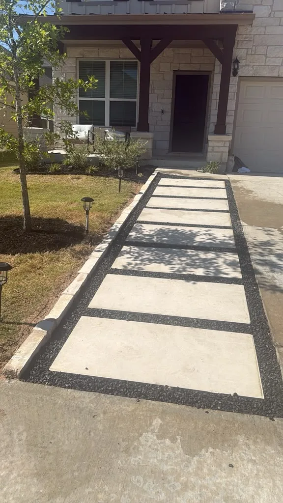 Front walkway of concrete pads with black gravel joints leading to a limestone house